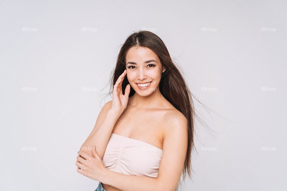 Beauty portrait of happy young beautiful asian woman with healthy dark long hair in top bando on white background isolated