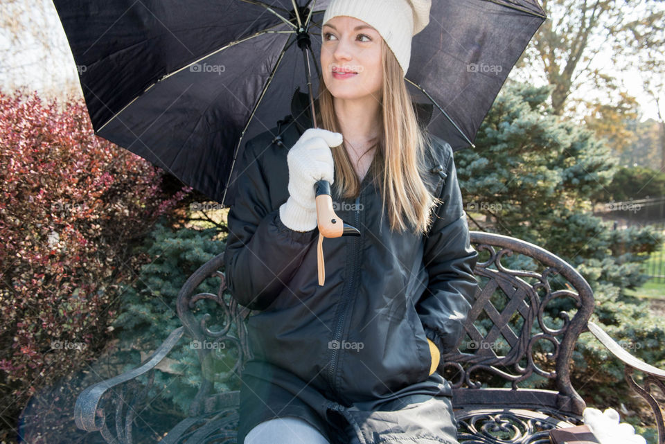 Young woman sitting on a bench outdoors while holding an umbrella