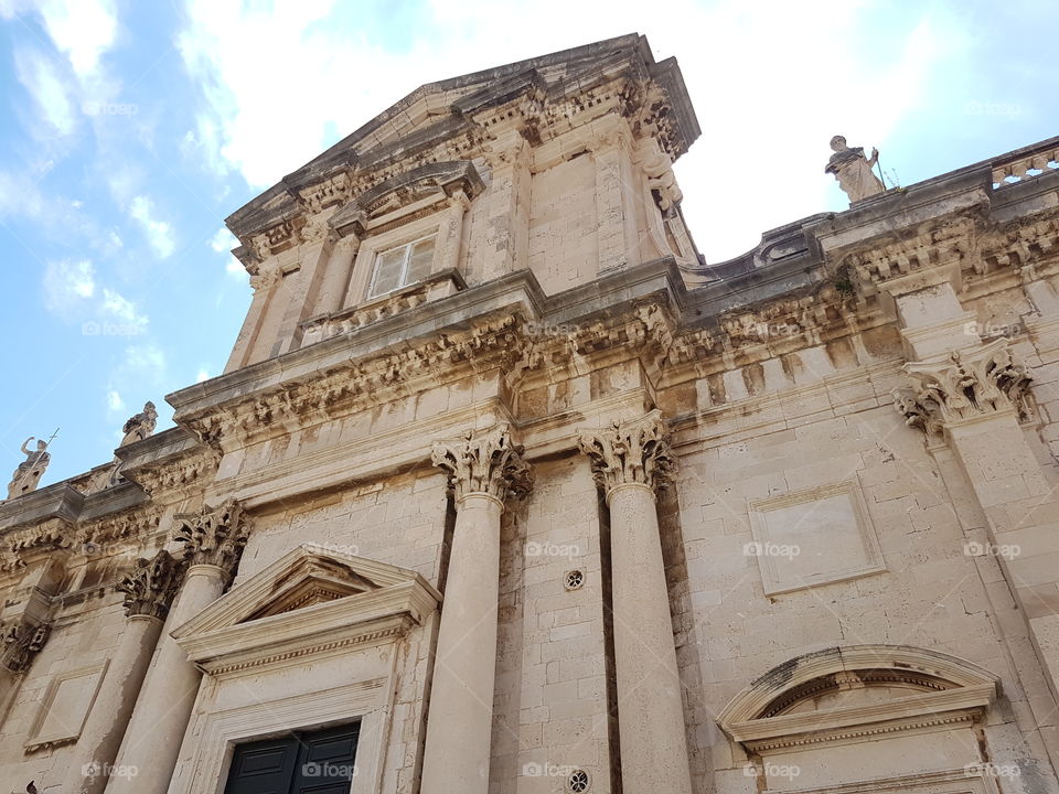 Looking up at old architectural building or church with sunny blue sky and clouds, traveling  in Dubrovnik, Croatia, Europe