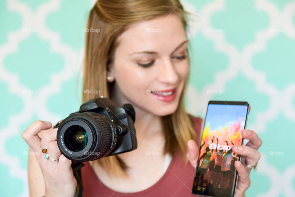 Young woman using the foap app on her phone and holding a DSLR camera