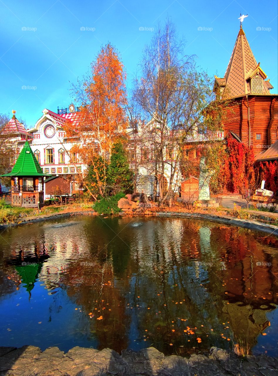 Reflection from the surface of the pond of autumn trees, old buildings, gazebos