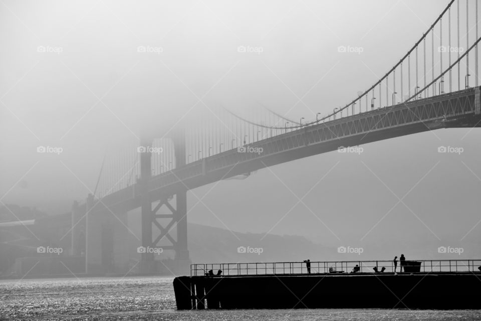 Mist covers the Golden Gate Bridge while fishermen enjoy the serenity of the sea. 