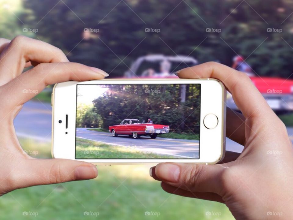 Using my mobile device to take a photograph of a vintage red car driving down the road