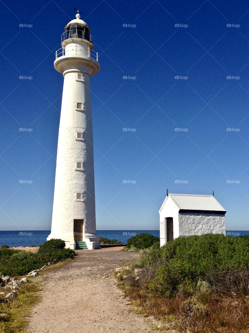 Bright White historic towering old stone lighthouse and building against brilliant South Australian blue sky and ocean backdrop, path leading up to it, Spencer Gulf, Point Lowly, near Whyalla 