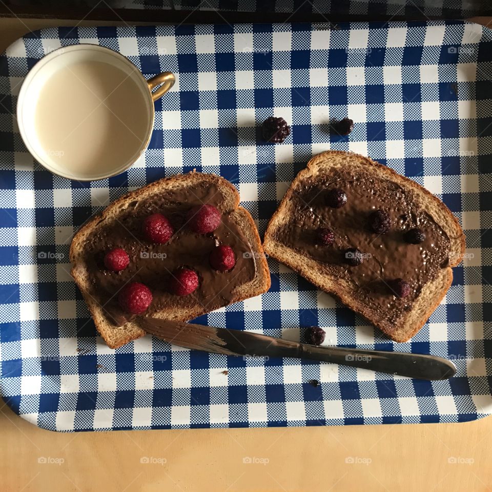 A yummy and delicious lunch time meal a Nutella chocolate sandwich with blackberries and raspberries served with a tea cup on a blue and white checkered tray. USA, America 