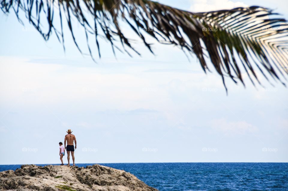 Rear view of a shirtless man standing near sea with child