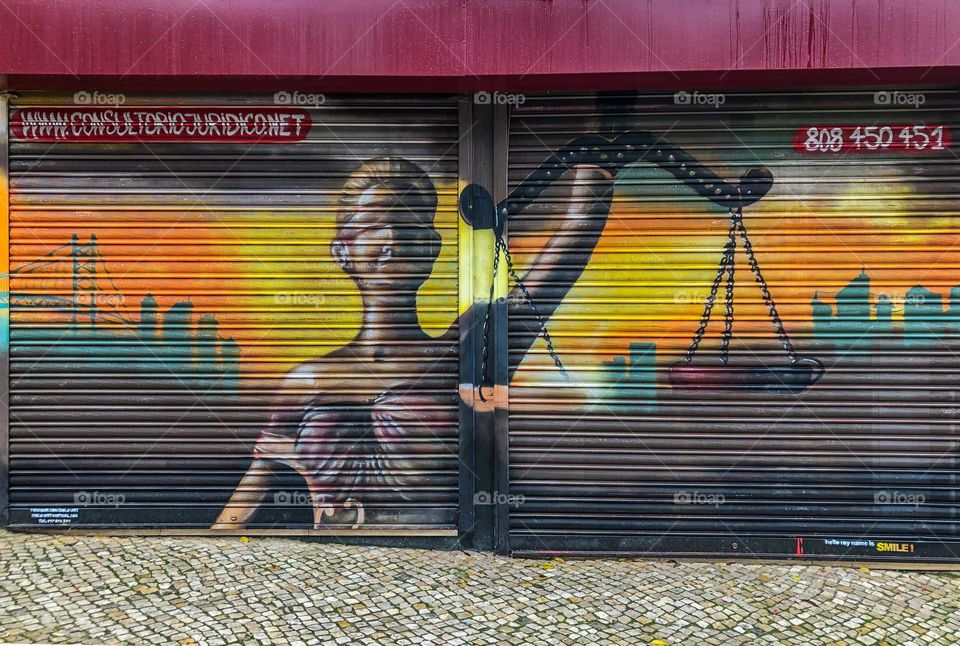 Blind justice - street art of blindfolded lady of liberty holding scales on metal shutters in Lisbon