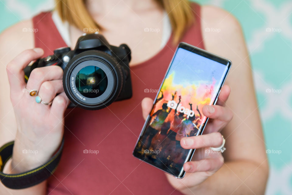 Close-up of a woman holding up her phone with the foap app displayed in one hand and holding her DSLR camera in the other