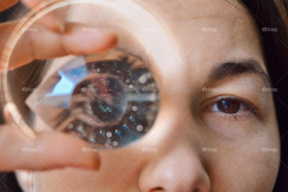 Light flare thru a tear shaped crystal held by a young woman against the eye