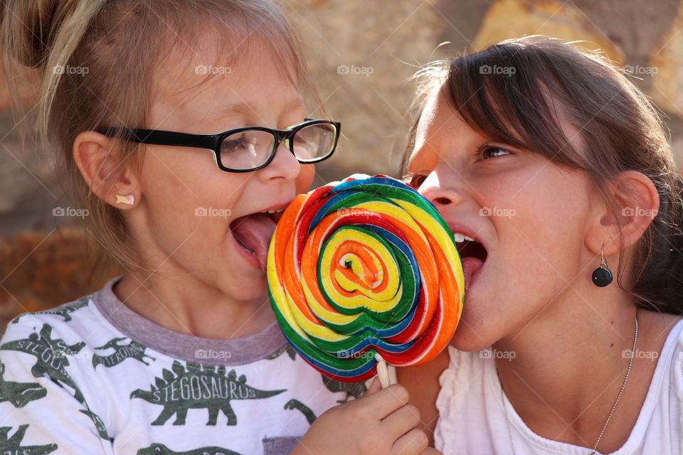 Two sisters sharing a lollipop
