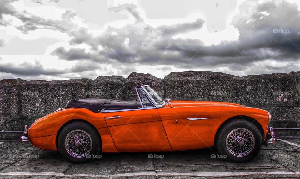 A red classic car on a stone harbour colour pop.