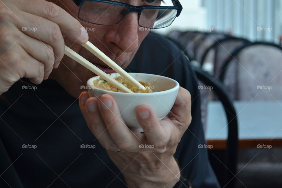 Man eating Asian Chinese food from bowl using chopsticks