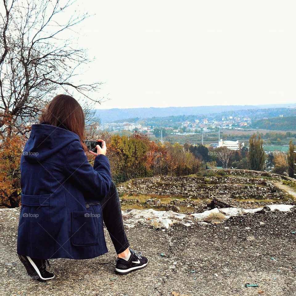 Beautiful view over some old roman ruins in a bulgarian village with a girl taking a photo of them in the autumn