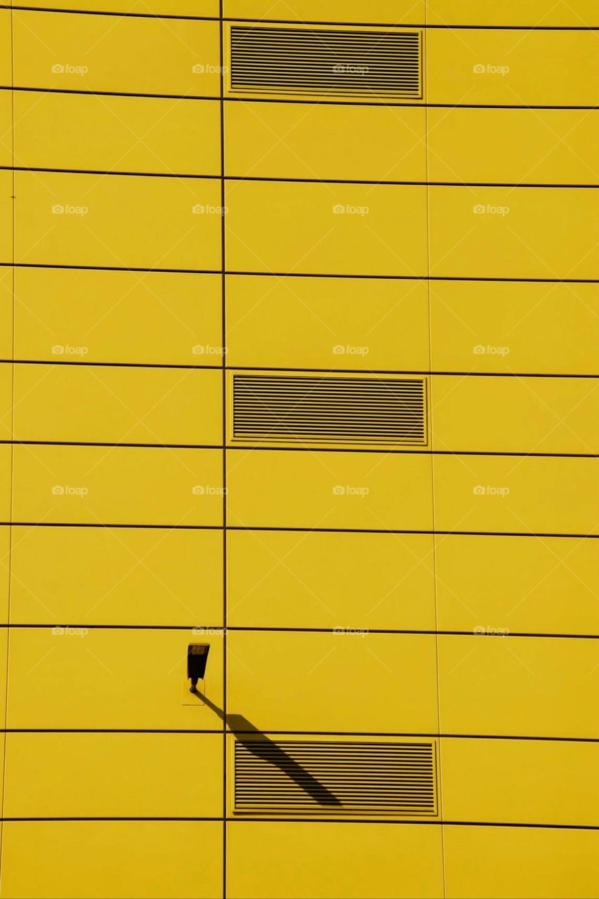 Yellow facade of an industrial building with a ventilation grille and a lamp in the sunlight