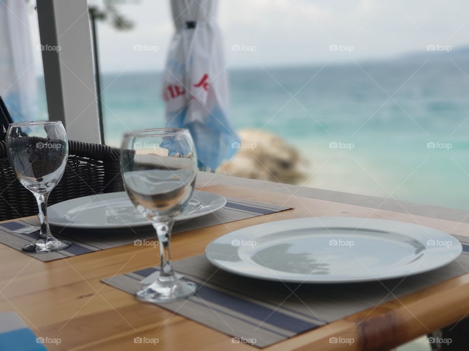 A few plates and a glass on a decorated table. it is a beautiful scenery right by the sea. you can truly feel all of the colours in the image and smell the wonderful arome of the Dalmatian Black Pine.