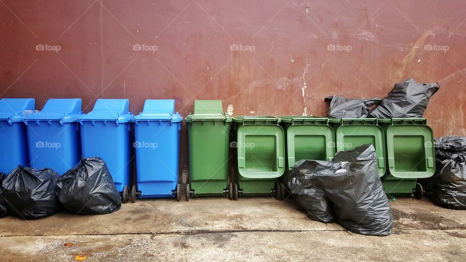 bright green and blue plastic recycle bins with black garbage bags on red cement wall background