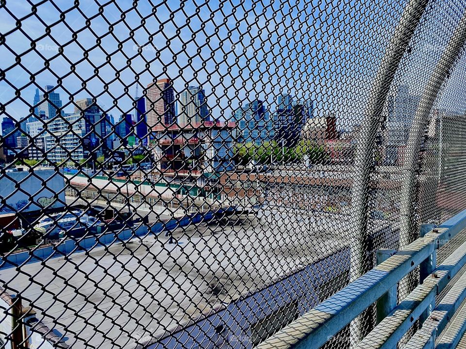 “Newtown Creek” is seen here through the mesh fence that protects pedestrians from the outside World while crossing the “Pulaski Bridge”. 2023. Hypnotic Productions