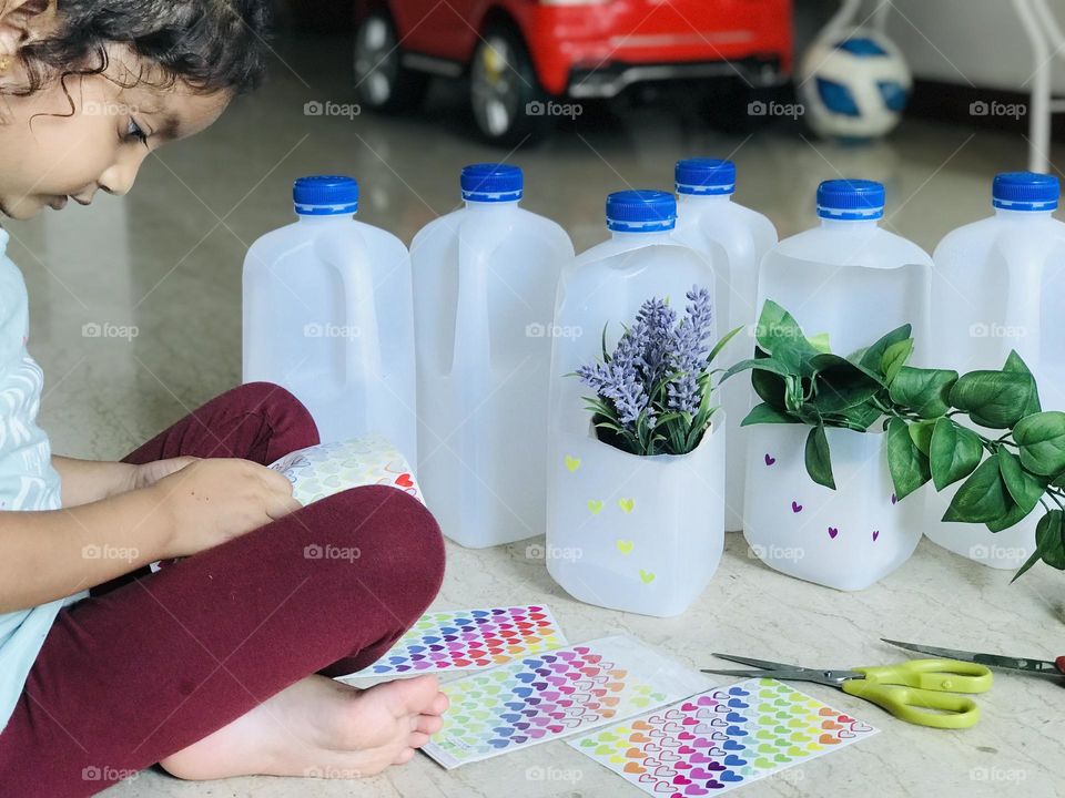 Girl pasting stickers on plastic milk bottles to make flower vases 