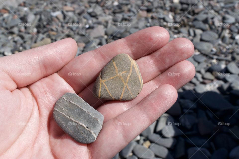 Striped stone and geometric stone held in hand with pebbles in background 