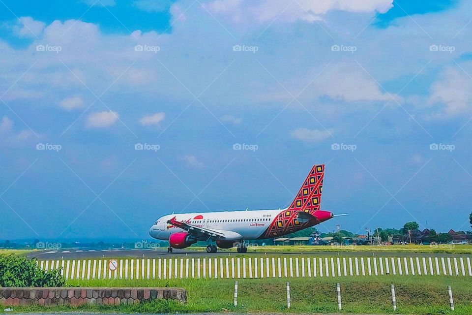 Long distance view of a plane with colorful motifs landing on the runway against a background of blue sky and white clouds