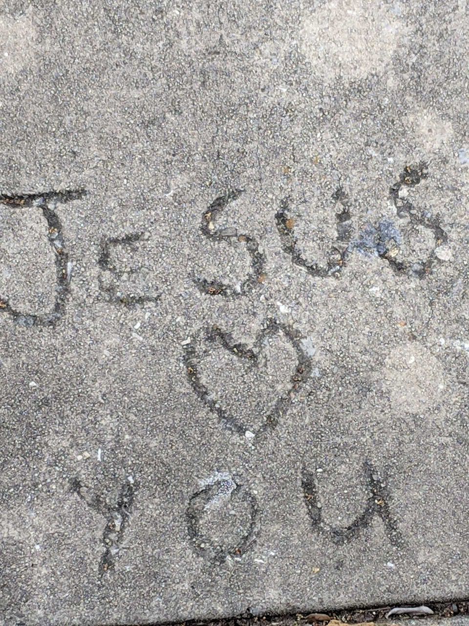 Jesus loves you drawn into the cement of an old sidewalk.