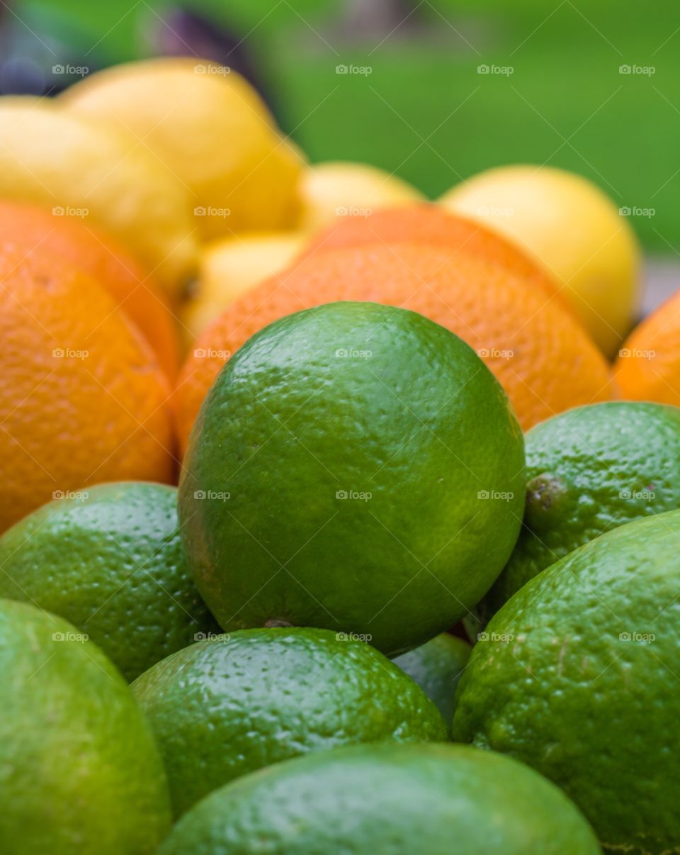 Vertical closeup photo of a bunch of limes, oranges and lemons with the limes in focus in the foreground