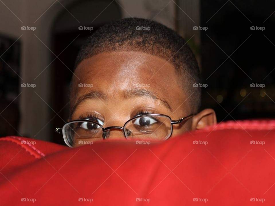 A youthful and jovial child partaking in a game of peekaboo behind a vibrant, fire engine red, leather couch.