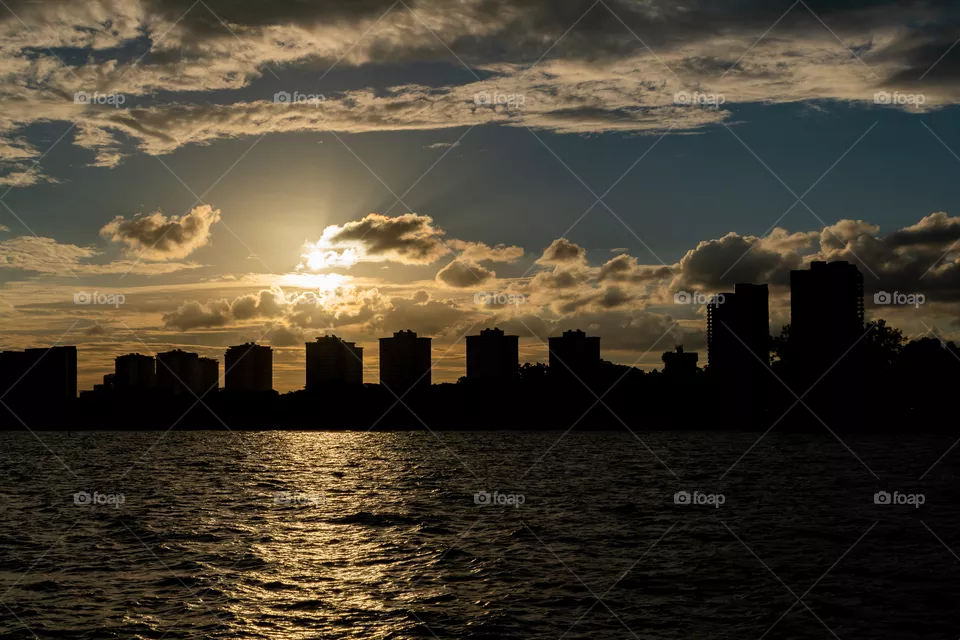 Sunset by the bay with cloudy blue sky and silhouette of buildings in the background