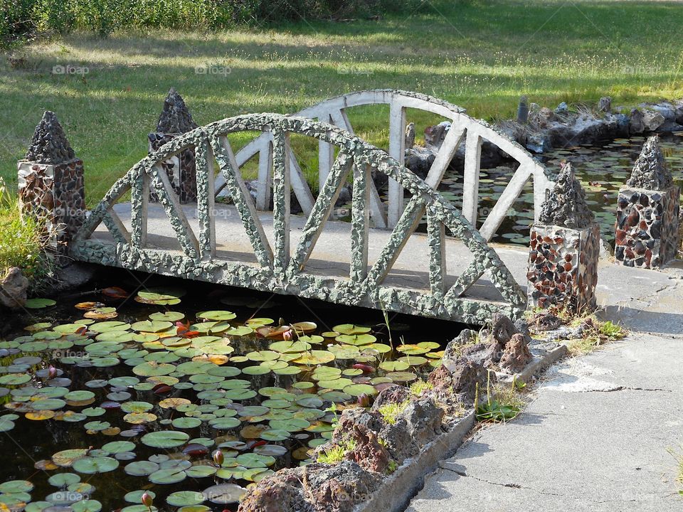A beautiful and ornate rock bridge on a peaceful path crosses a fairytale style mote with lots of Lillie Pads at Peterson’s Rock Garden on a sunny summer day in Central Oregon.