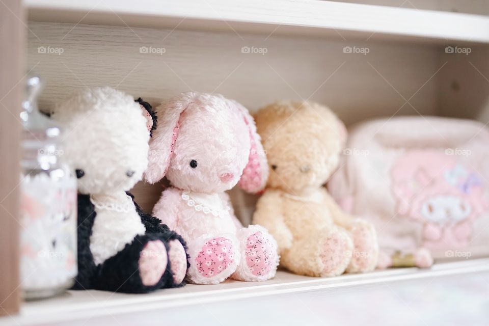 Cute soft plushes. Lovely dolls are sitting on the little girl's headboard and other cute accessories. Selective focus on kawaii pink bunny doll soft plush.