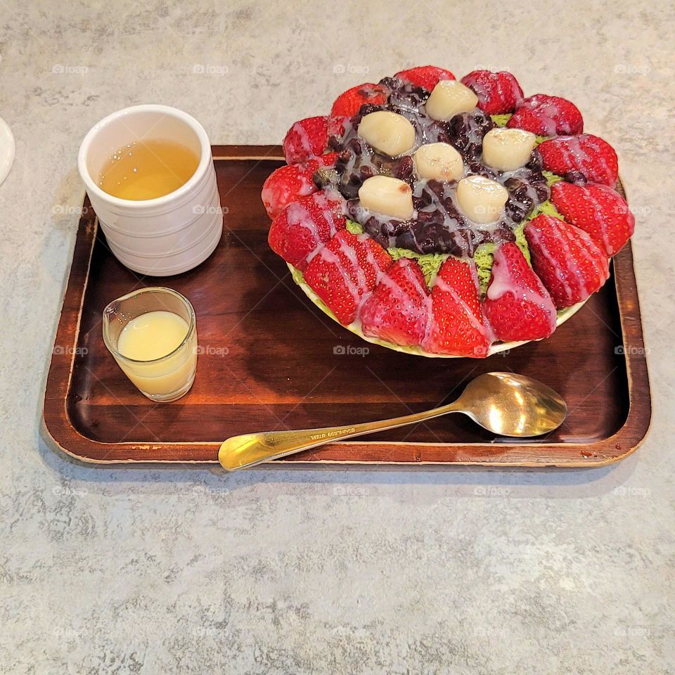 Matcha flavored shaved ice with strawberries, dangos and sweet red beans, topped with condensed milk, and paired with green tea to relieve fatigue.