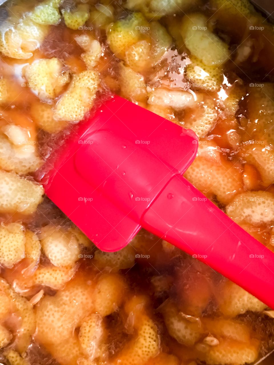 Red spatula stirring lemon rinds, brown sugar, juice, for lemonade syrup closeup background