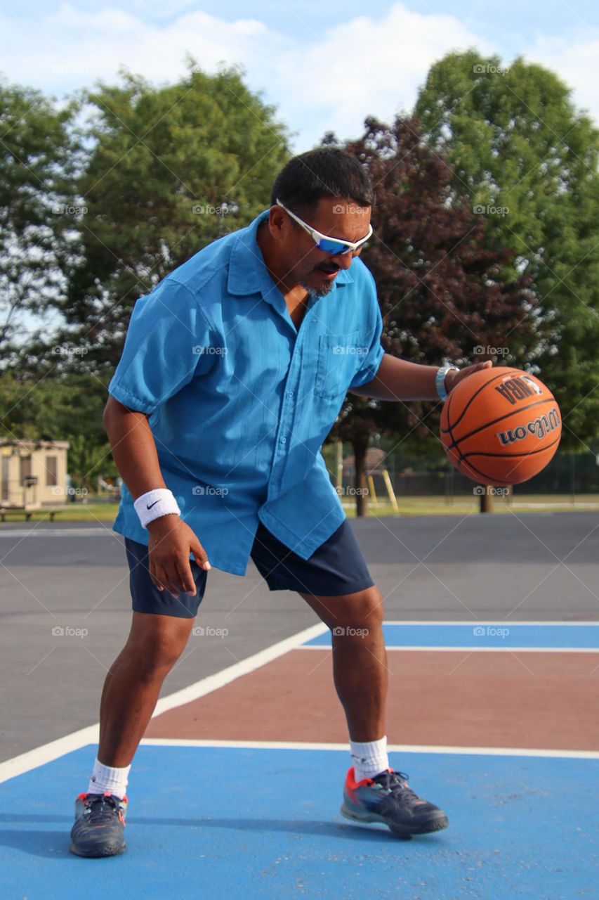 Middle-aged man is playing basketball outdoors