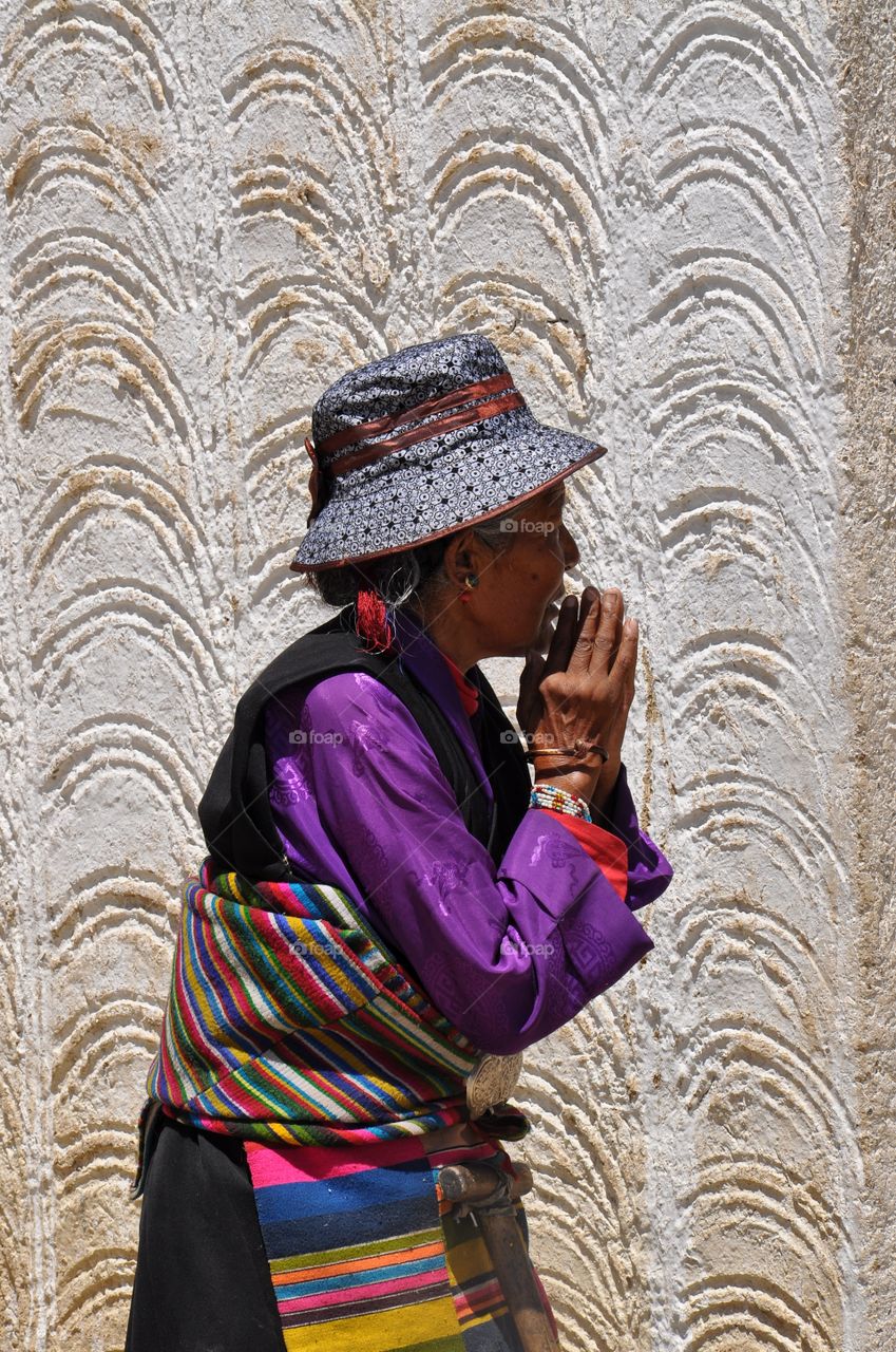 tibetan woman in traditional clothes making kora around buddhist monastery and praying