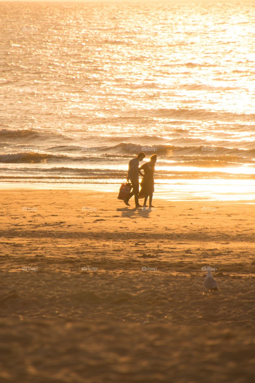 A couple walking in the sand on the beach during a gorgeous sundown 