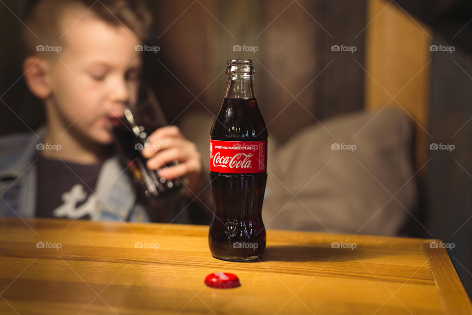 kid of seven years old drinking delicious Coca-Cola in a restaurant.  Cola bottle is on the table