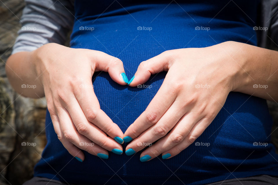 pregnant woman holds heart shaped hands on belly