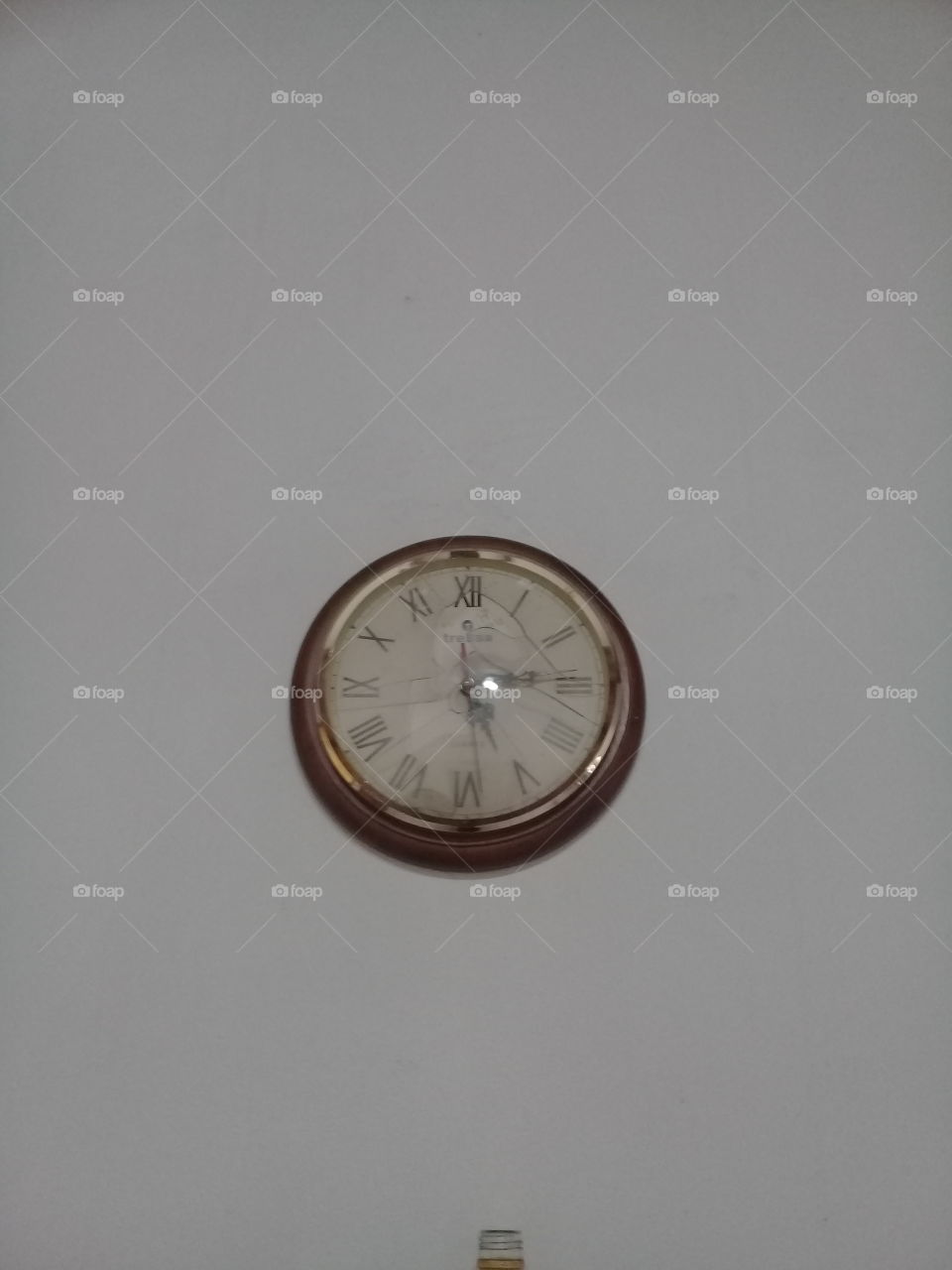 antiguo reloj de pared con marco de madera lustrada y agujas de metal, colgado sobre pared de cemento pintada de blanco
