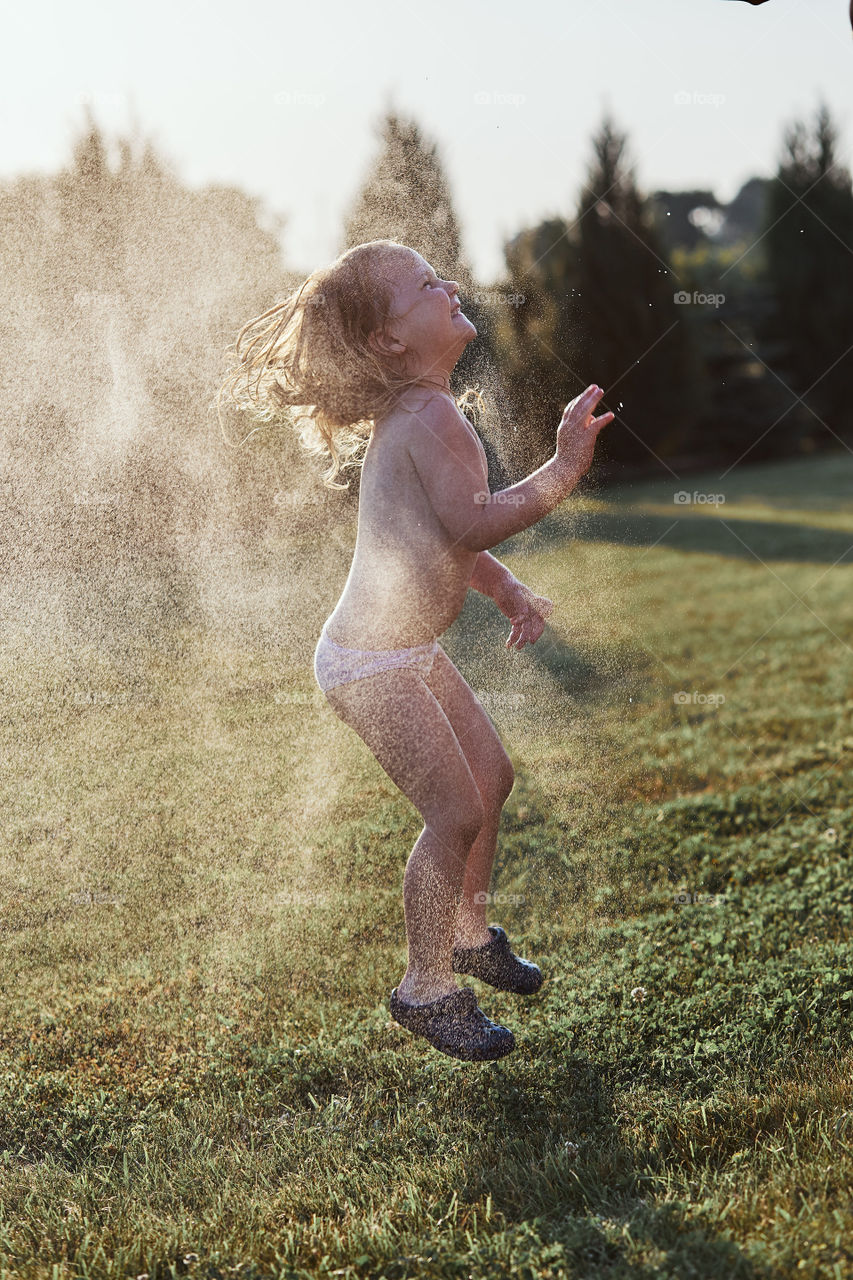 Little cute adorable girl enjoying a cool water sprayed by her father during hot summer day in backyard. Candid people, real moments, authentic situations