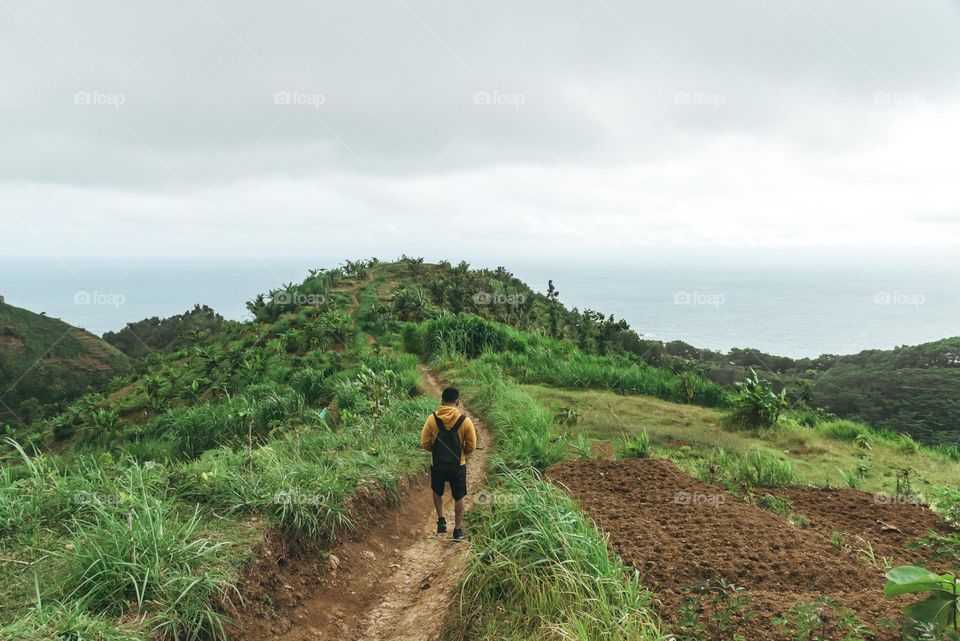 A man walks on a beautiful meadow up on the hills with the view of sea in front of him