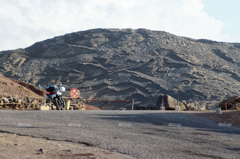 Motorcycle parked next to a giant lava rock. In El Golfo, Lanzarote. (Lago Verde).