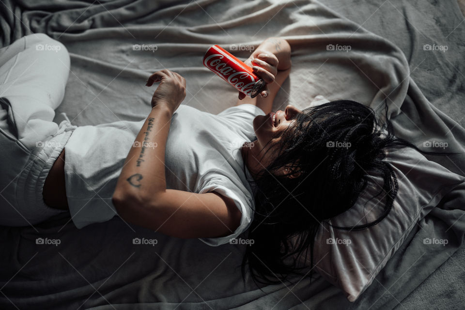 the girl lies on the bed and holds a Coca Cola