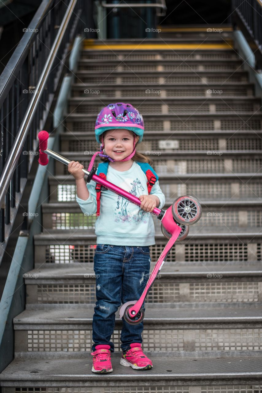 Smiling girl holding scooter standing on staircase