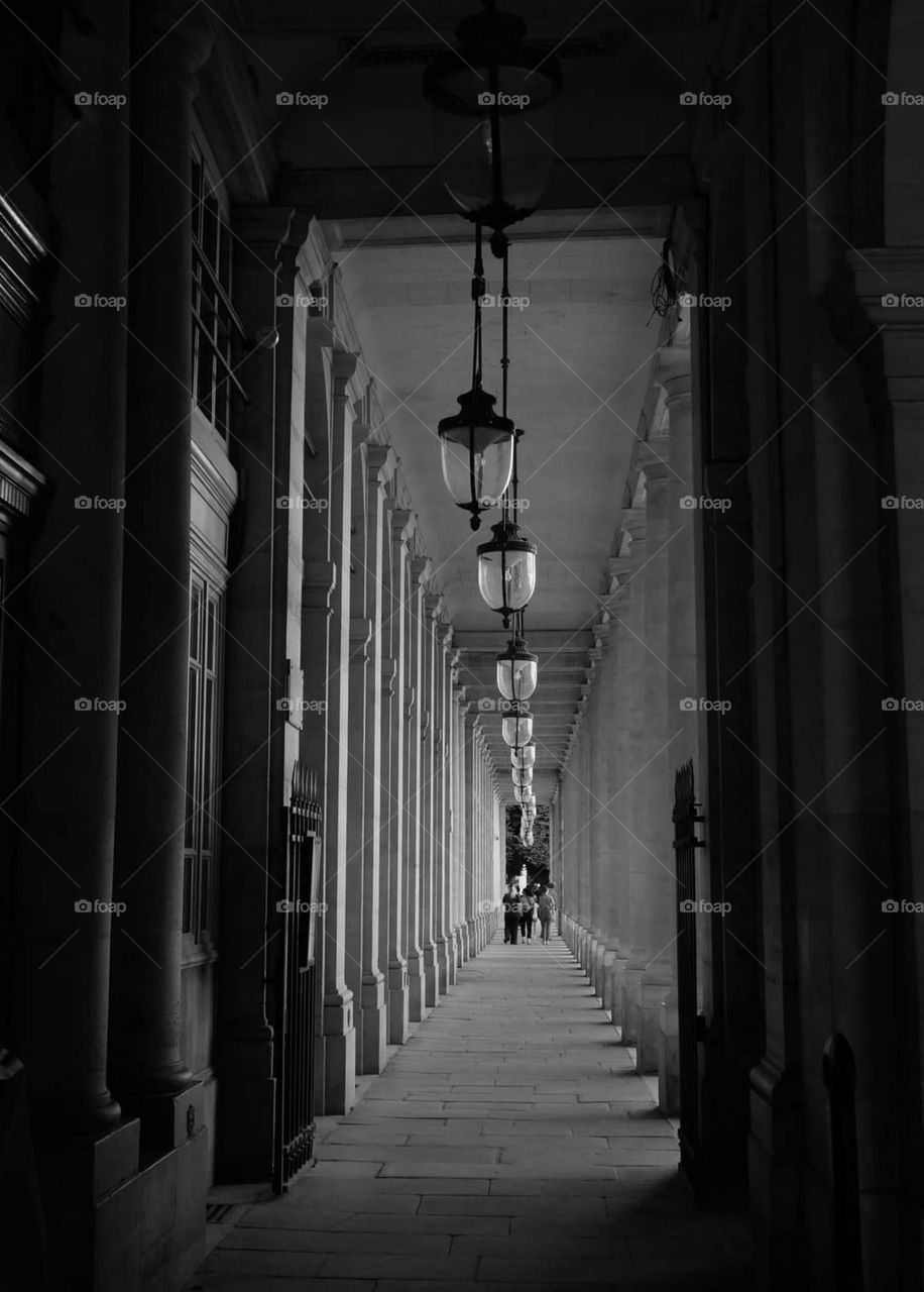 Black & white shot of the suspended lanterns of the column-lined alley, called "les colonnades" of the Royal Palace in Paris