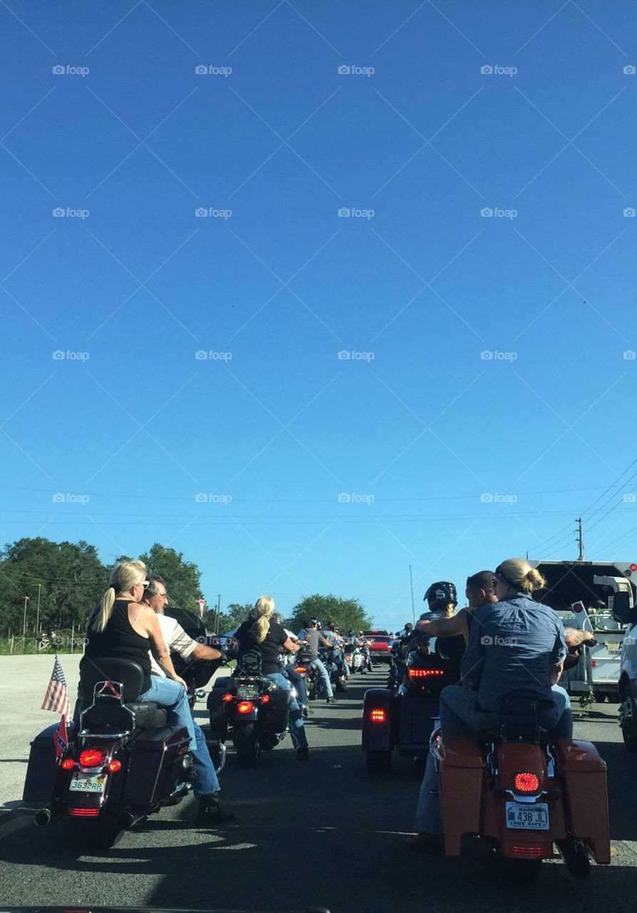 Motorcyclists in Daytona Beach and Ormond Beach Florida during Biketoberfest biker festival. Rear view with men and women riding Harley Davidson, Honda, BMW motorbikes, trikes and 3-wheelers. Bikers wait at light with line of cars, views from behind. 