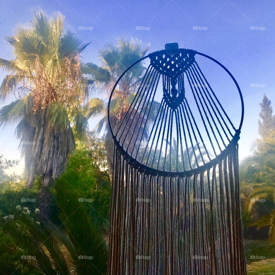 A dream catcher in the window in front of a tropical setting with palm trees and blue skies USA,America