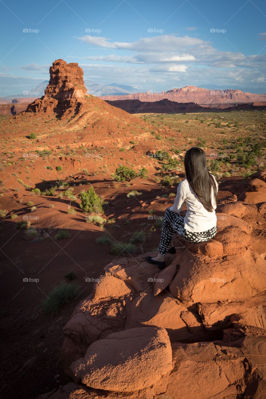 Girl looking butte in morning. Dark haired girl admiring desert scenery during sunrise. Sandstone butte. Mountains. Desert. White clothes. Clouds