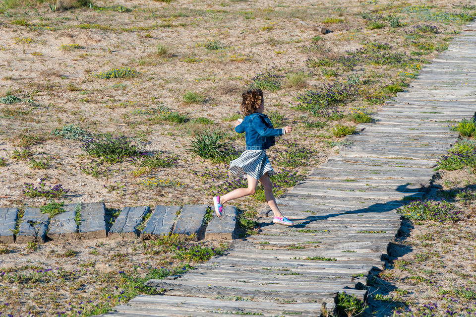 Little girl running on wooden footpath.