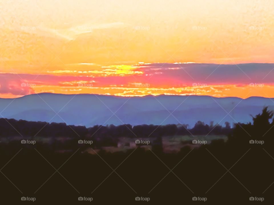 The golden sun is setting on another evening over the majestic Blue Ridge Mountains splashing vivid colors of yellow, orange, purple, and pink across the sky.