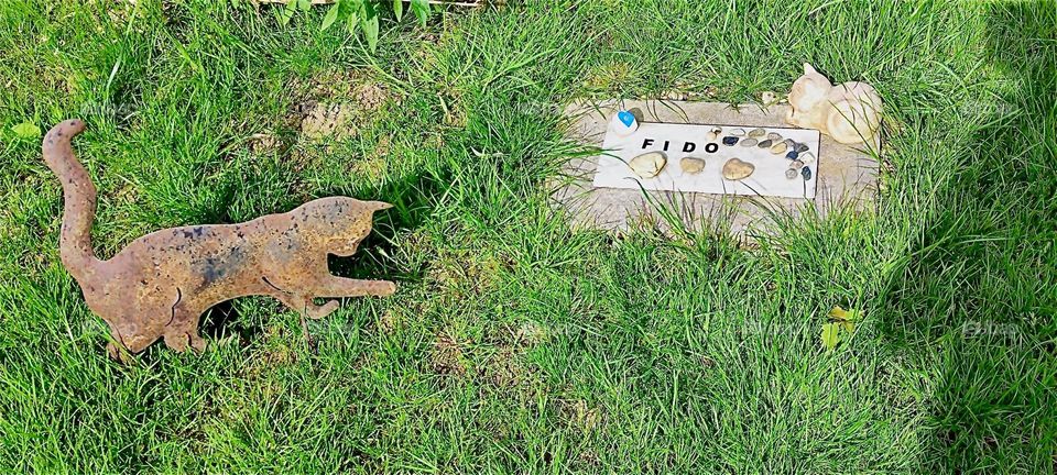 The stone on the lawn next to the feline garden sculpture marks the grave of “Fido”, the fifteen year old tomcat who passed away more than two years ago. 2024. Hypnotic Productions